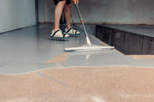 A construction worker applying grey epoxy resin in an industrial hall