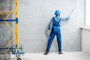 Plasterer in blue working uniform plastering the wall indoors