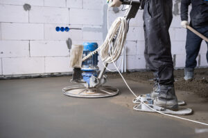 Ramming and grinding of semi-dry floor screed by a machine with a rotating disk for leveling. Construction of a concrete floor in the house, a master with special equipment.