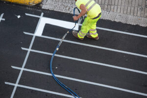 Worker painting a pedestrian crosswalk road using paint sprayer gun